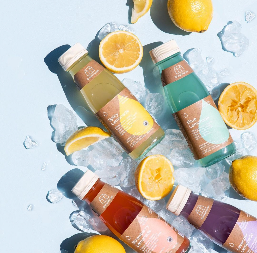 Lemonades placed on a light blue background with lemons and crushed ice positioned around them.