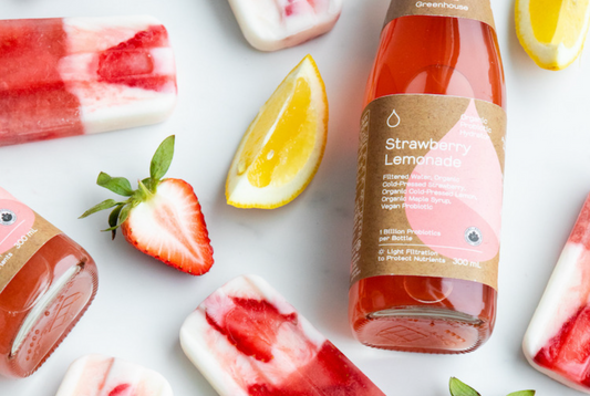 A bottle of strawberry lemonade lying among popsicles, strawberry slices, and lemon slices