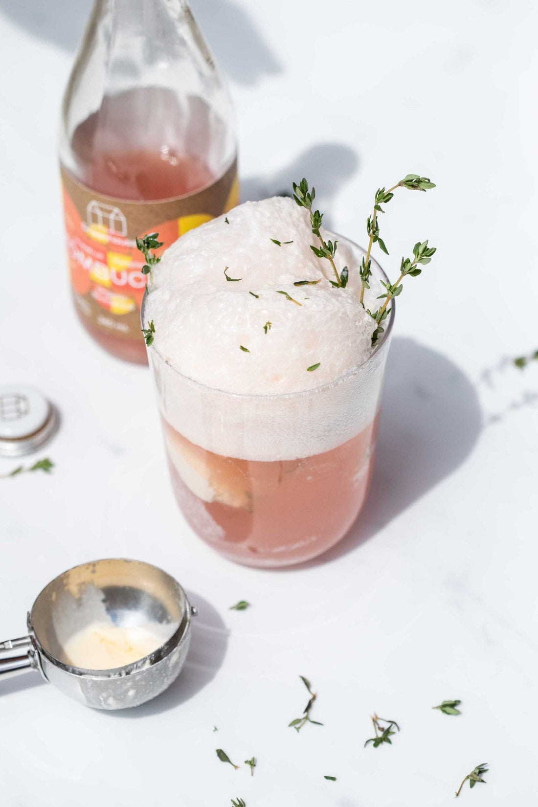 A light pink drink with froth on top, garnished with green sprigs. 