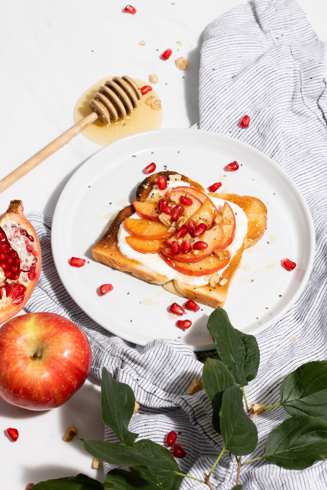 A top-down view of a slice of toast piled with apples, yogurt, and pomegranate seeds.